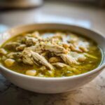 Close-up of a white bowl filled with Instant Pot Chicken Pozole Verde, featuring shredded chicken and white beans in a vibrant green broth.