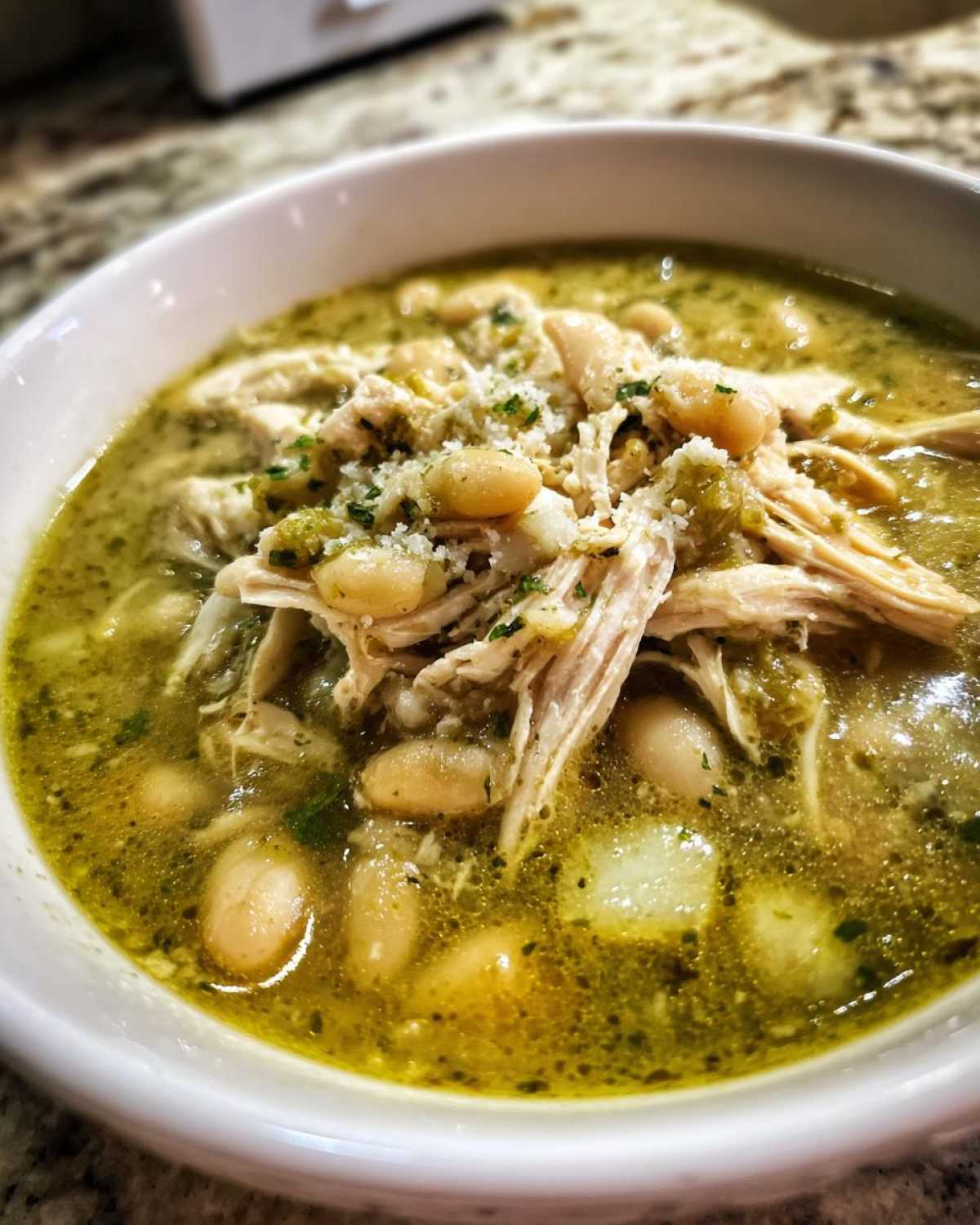 Close-up of a white bowl filled with Instant Pot Chicken Pozole Verde, featuring shredded chicken, white beans, and green broth.