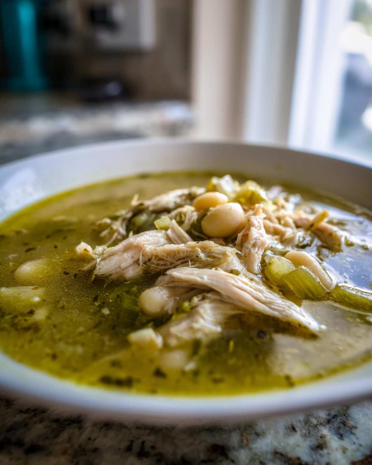 Close-up of shredded chicken and white hominy beans in a bowl of green broth for Instant Pot Chicken Pozole Verde.