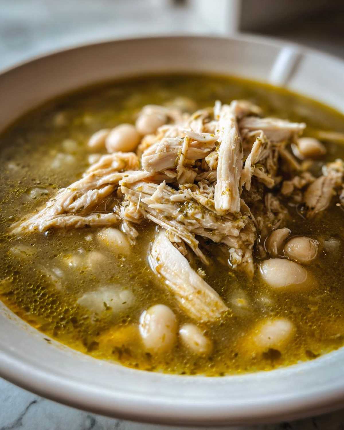 A close-up, appetizing bowl of Instant Pot Chicken Pozole Verde featuring shredded chicken and white hominy beans in a green broth.