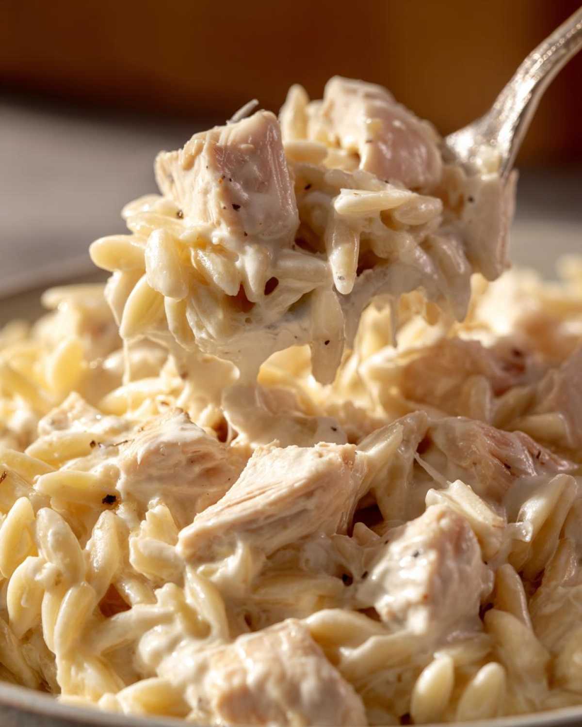 A close-up of a spoonful lifting creamy Instant Pot Creamy Chicken and Orzo from a bowl, showing chunks of chicken and rich sauce.