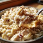 A spoonful of creamy Instant Pot Creamy Chicken and Orzo being lifted from a bowl, showing rich sauce and orzo pasta.