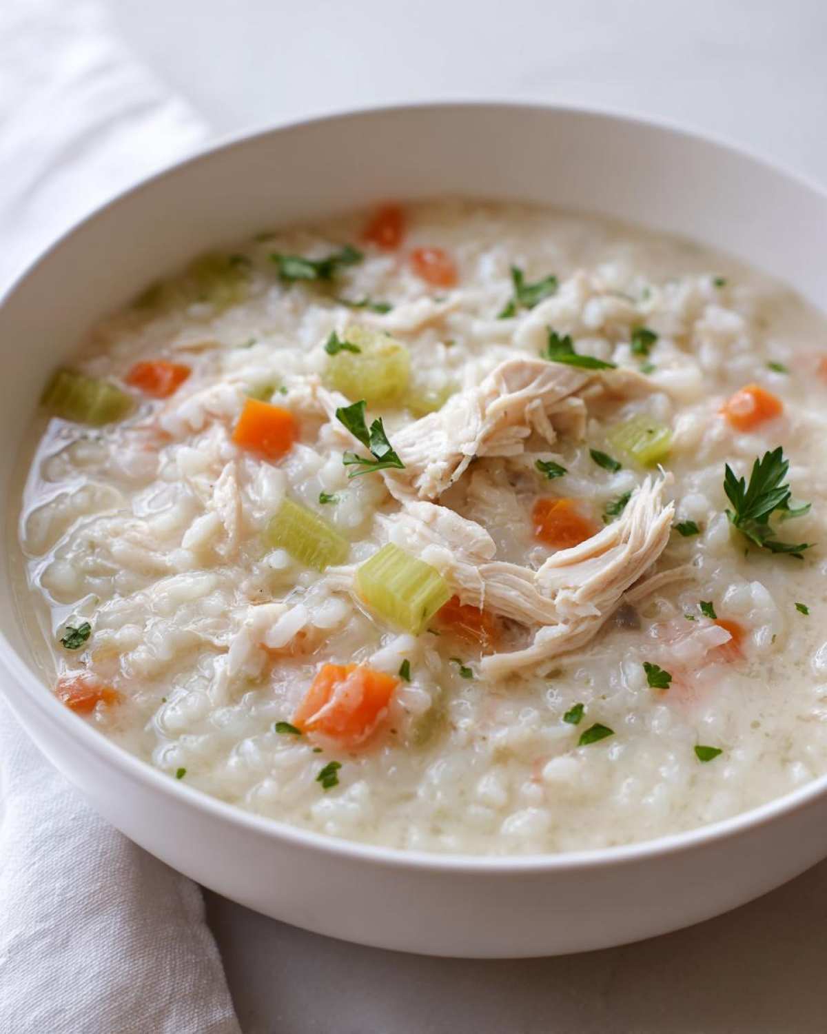 A close-up view of a white bowl filled with Instant Pot Creamy Chicken and Rice Soup, topped with shredded chicken and parsley.