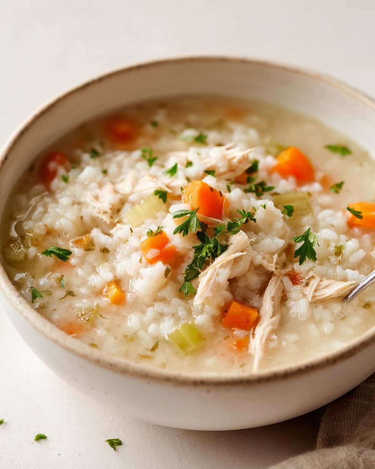 Close-up of a bowl of Instant Pot Creamy Chicken and Rice Soup with shredded chicken, rice, carrots, and parsley garnish.