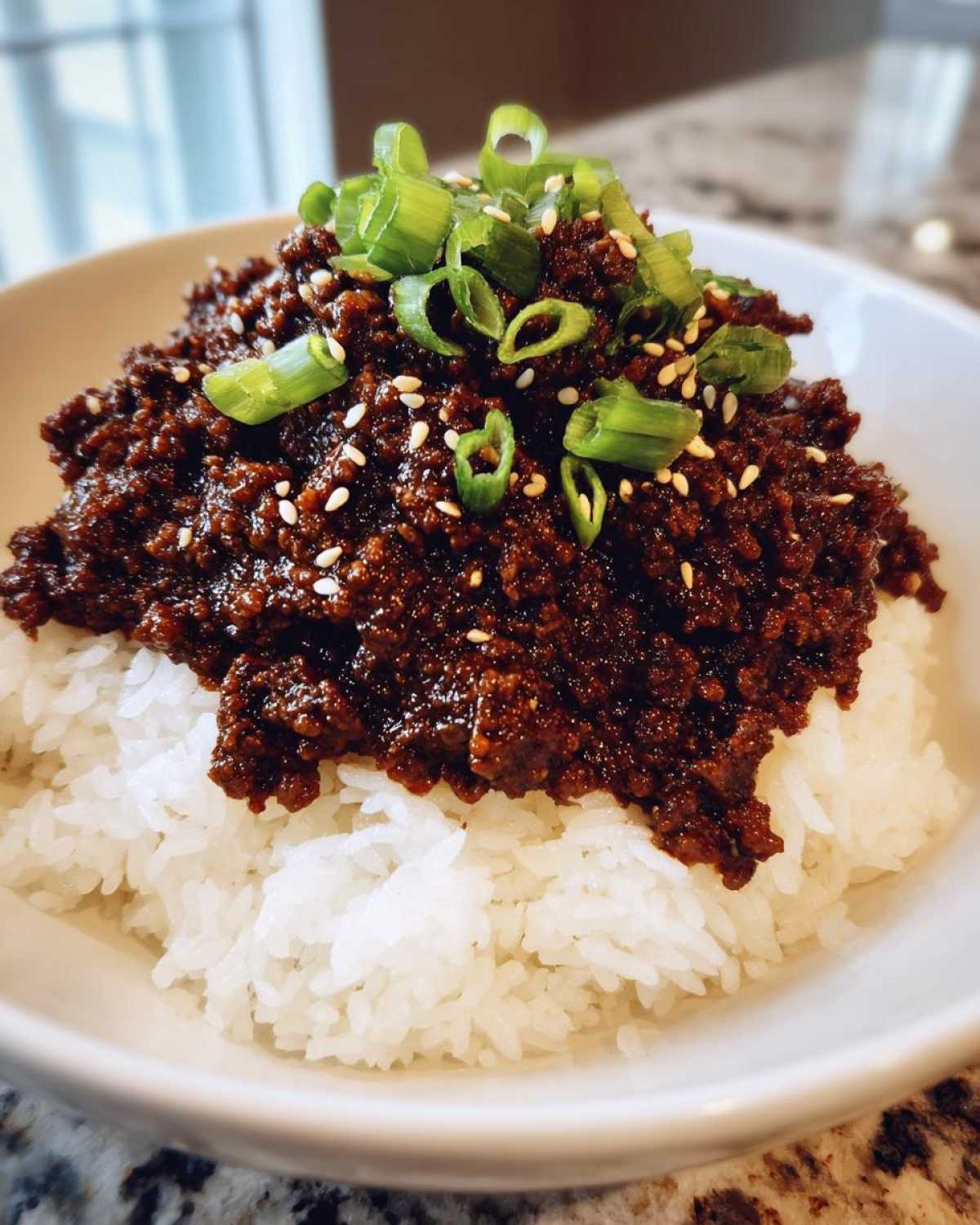 Close-up of a white bowl filled with white rice topped generously with saucy Instant Pot Korean Beef and garnished with green onions and sesame seeds.