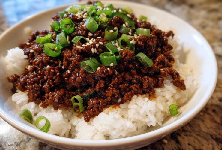 A close-up of a white bowl filled with white rice topped generously with saucy Instant Pot Korean Beef and garnished with green onions and sesame seeds.