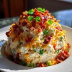 A mound of creamy jalapeno popper chicken salad topped generously with shredded cheese, bacon bits, and green onions.