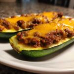 Two halves of Keto Cheesy Taco Stuffed Zucchini Boats filled with seasoned ground meat and melted cheddar cheese, served on a white plate.