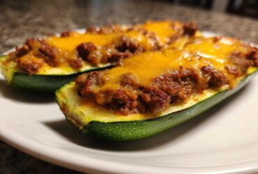 Two halves of Keto Cheesy Taco Stuffed Zucchini Boats filled with seasoned ground meat and melted cheddar cheese, served on a white plate.