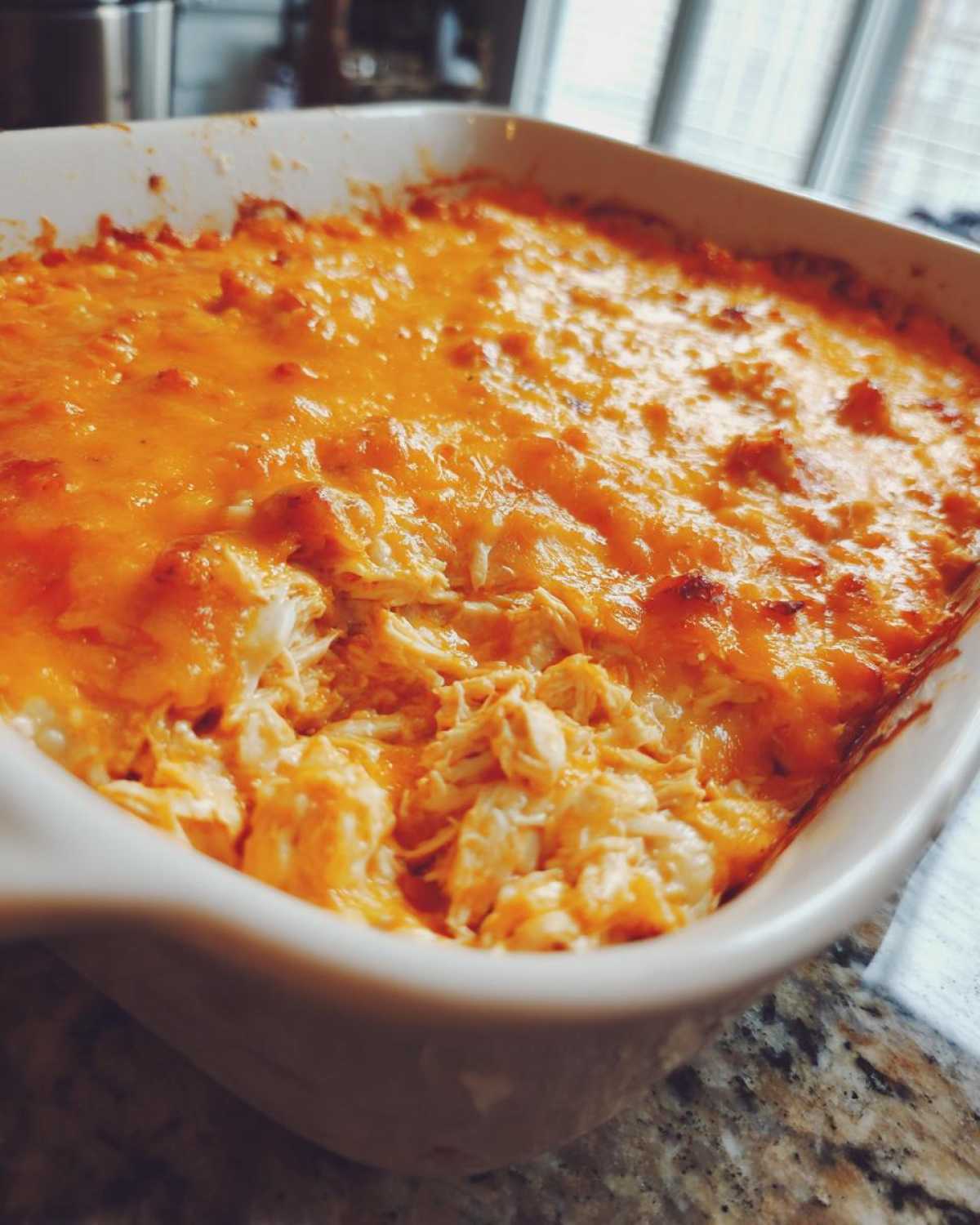 Close-up of a baked Keto Creamy Buffalo Chicken Casserole topped with melted orange cheddar cheese.