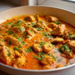Close-up of Keto Creamy Butter Chicken Skillet with tender chicken pieces in a rich, orange sauce, garnished with fresh cilantro.