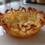 A close-up of a single, golden-brown, crispy Keto Crispy Cheese Taco Shell Bowl resting on a white plate.