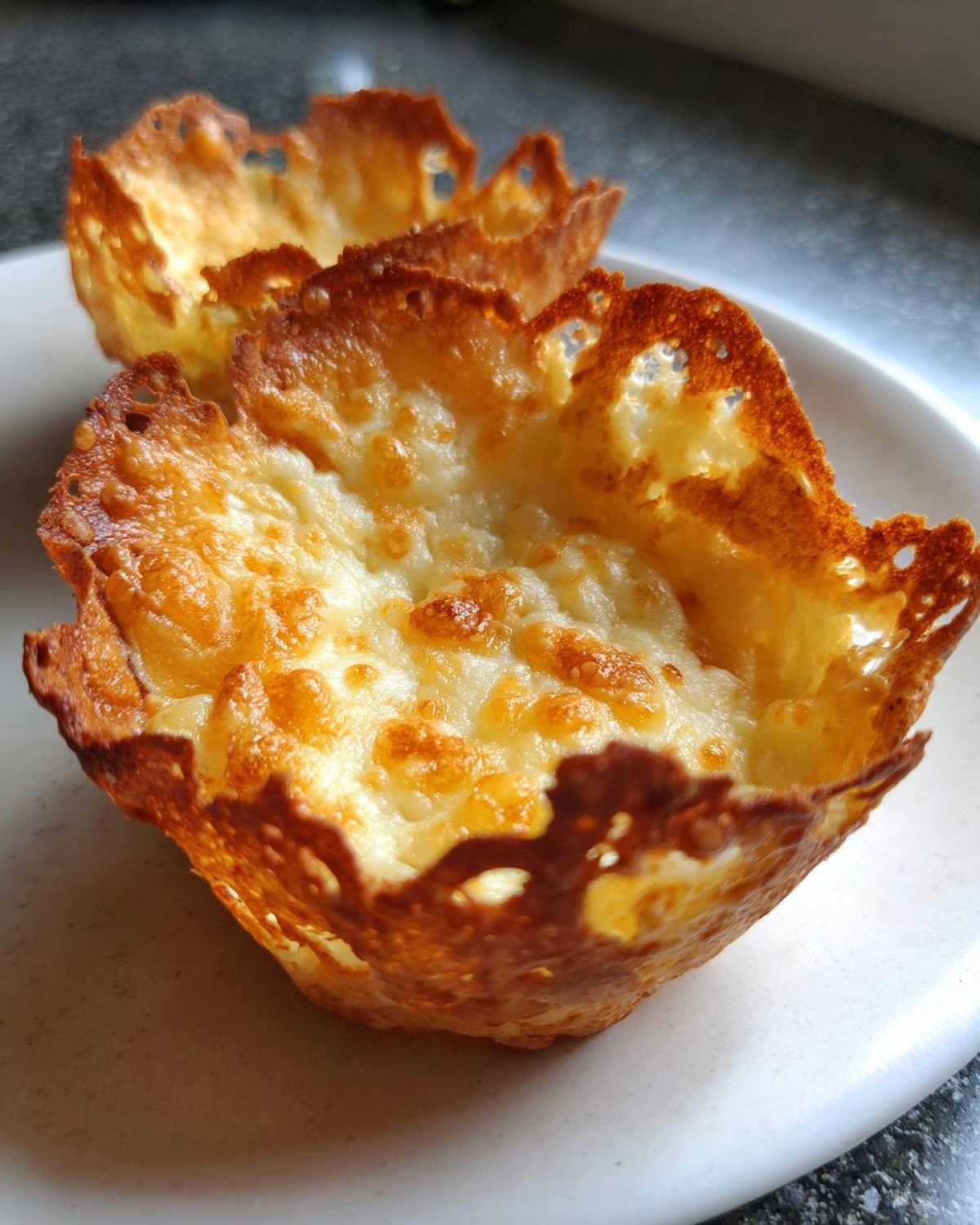 Close-up of two golden-brown, crispy Keto Crispy Cheese Taco Shell Bowls resting on a white plate.