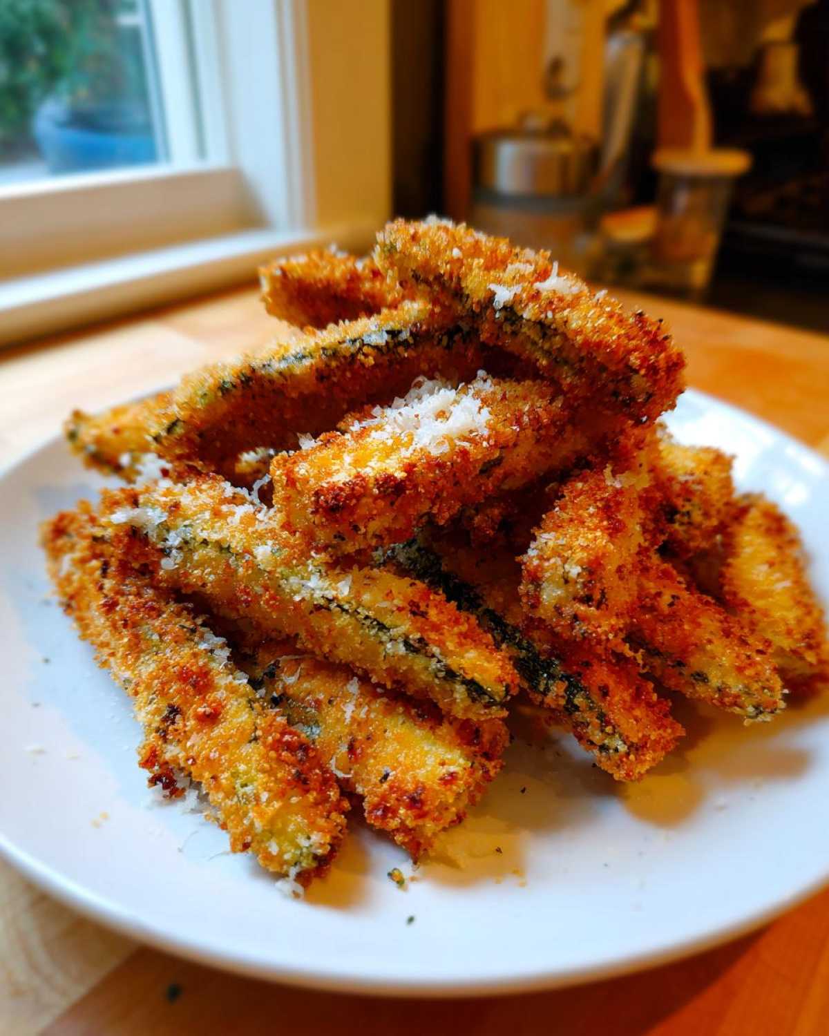 A close-up of a pile of golden brown Keto Crispy Parmesan Zucchini Fries sprinkled with extra cheese.