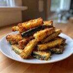A tall stack of golden brown Keto Crispy Parmesan Zucchini Fries piled high on a white plate.