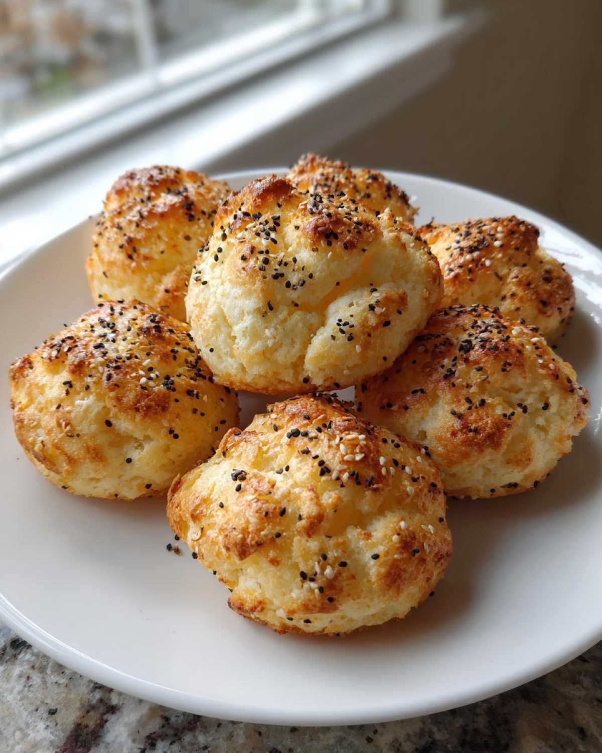Six golden brown Keto Everything Bagel Cloud Bread buns topped with black and white sesame seeds on a white plate.
