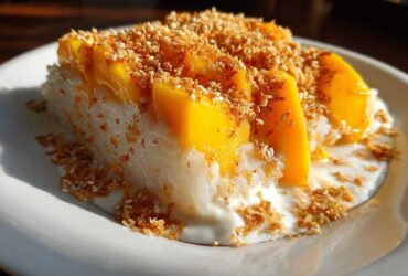 A close-up of a serving of mango sticky rice, topped with fresh mango slices and toasted sesame seeds.