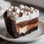 Close-up of a rich slice of Mississippi Mud Pie showing four distinct layers and topped with whipped cream and mini marshmallows.