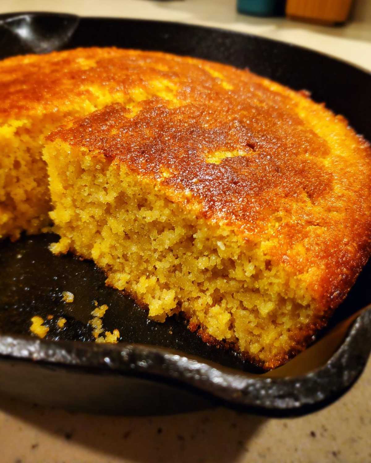 Close-up of a slice removed from moist cornbread with a golden-brown crust, baked in a black cast iron skillet.