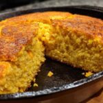 Close-up of moist, golden cornbread with a dark, crispy crust, cut open in a black cast iron skillet.