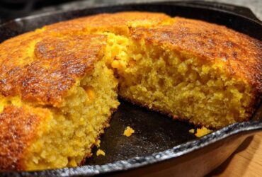 Close-up of moist, golden cornbread with a dark, crispy crust, cut open in a black cast iron skillet.