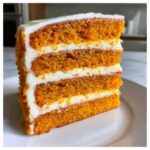 Close-up of a tall slice of Creamsicle Cake with four vibrant orange layers separated by thick white frosting.