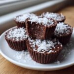 A stack of five No-Bake Chocolate Coconut Protein Cups topped with shredded coconut on a white plate.