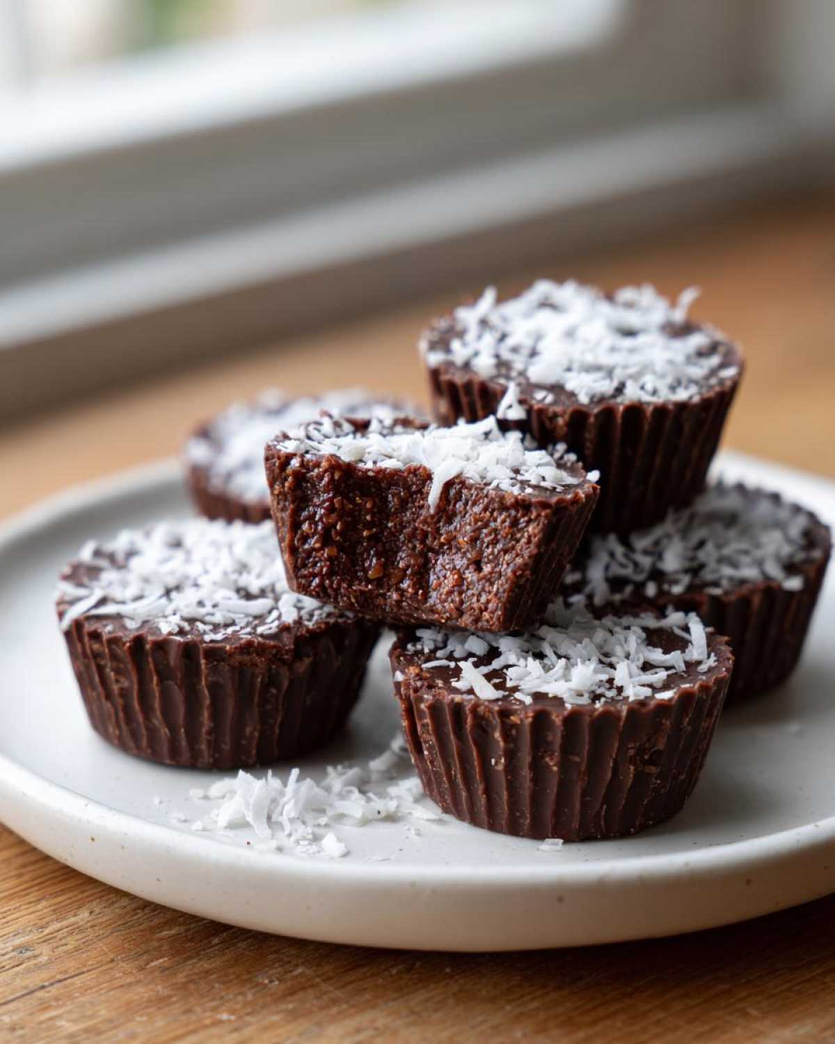 A stack of five rich, dark No-Bake Chocolate Coconut Protein Cups topped with shredded coconut.