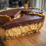 A close-up slice of no-bake chocolate peanut butter pie showing the thick peanut butter filling and chocolate ganache topping.