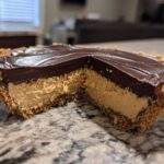 A close-up cross-section view of a no-bake chocolate peanut butter pie with a graham cracker crust, creamy filling, and chocolate topping.