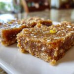 Three squares of dense, chewy No-Bake Lemon Almond Date Bars topped with white almond pieces and lemon zest.