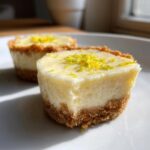 Two No-Bake Lemon Cream Pie Cups with a graham cracker crust and lemon zest topping, one with a bite taken out.