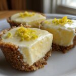 Three No-Bake Lemon Cream Pie Cups on a white plate, featuring a thick graham cracker crust and bright yellow lemon filling topped with zest.