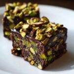 Two rich squares of No-Bake Pistachio Chocolate Fudge Squares topped with chopped pistachios on a white plate.