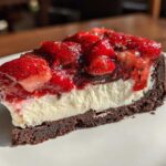 A close-up view of a No-Bake Strawberry Chocolate Cheesecake Slice featuring a dark crust, creamy filling, and glossy strawberry topping.