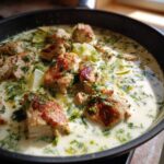 Close-up of seared chicken pieces simmering in a creamy coconut lime sauce with fresh herbs and lime wedges.
