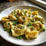 A close-up of One-Pot Creamy Garlic Butter Tortellini and Peas served on a white plate, garnished with herbs.