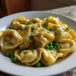 A close-up of a white bowl filled with One-Pot Creamy Garlic Butter Tortellini and Peas, topped with herbs and pepper.