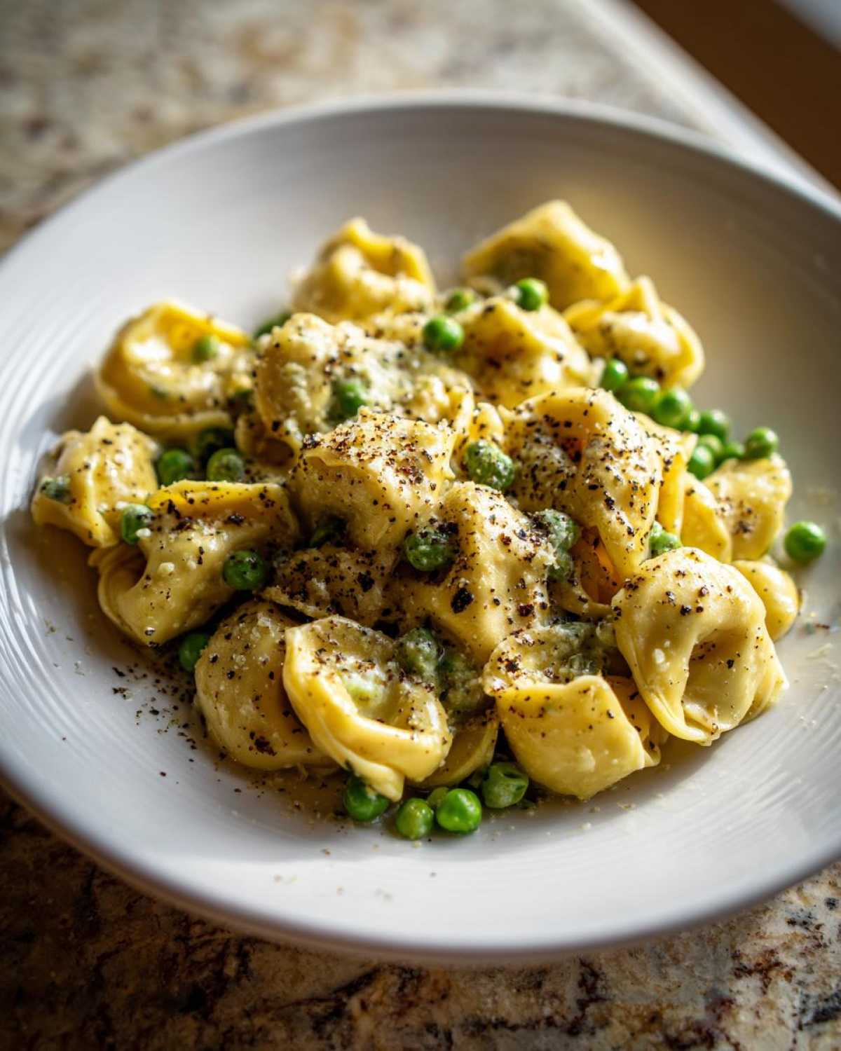 A close-up of One-Pot Creamy Garlic Butter Tortellini and Peas served in a white bowl, generously topped with black pepper.