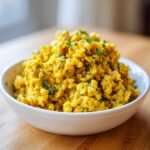 Close-up of a white bowl filled with bright yellow One-Pot Creamy Lemon Garlic Farro, garnished with fresh parsley.