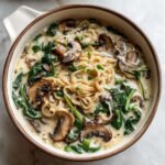 A close-up overhead shot of a bowl of One-Pot Creamy Mushroom Spinach Ramen featuring noodles, sliced mushrooms, and wilted spinach in a rich broth.