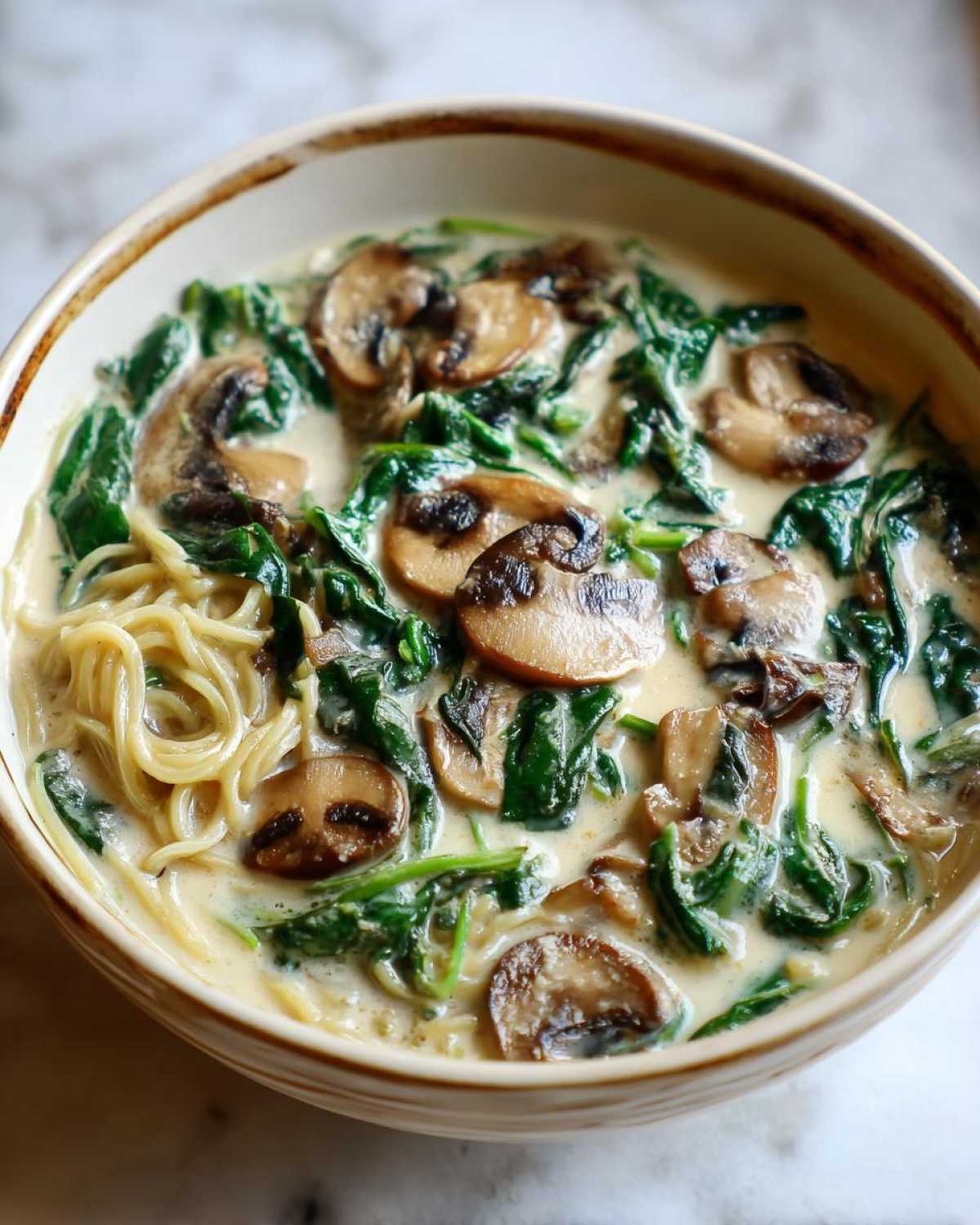 A close-up of a bowl of One-Pot Creamy Mushroom Spinach Ramen, featuring noodles, sliced mushrooms, and wilted spinach in a rich broth.
