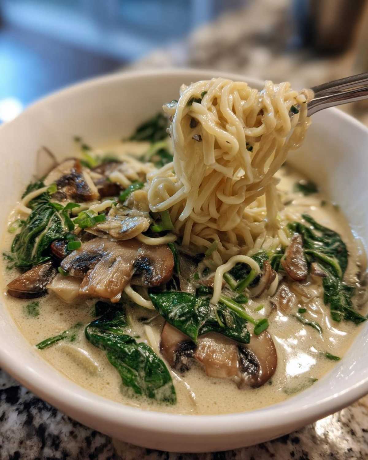 A fork lifts noodles from a bowl of One-Pot Creamy Mushroom Spinach Ramen, showing rich broth, mushrooms, and spinach.