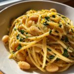 A close-up of a bowl of One-Pot Creamy White Bean Lemon Pasta topped with fresh parsley and lemon zest.