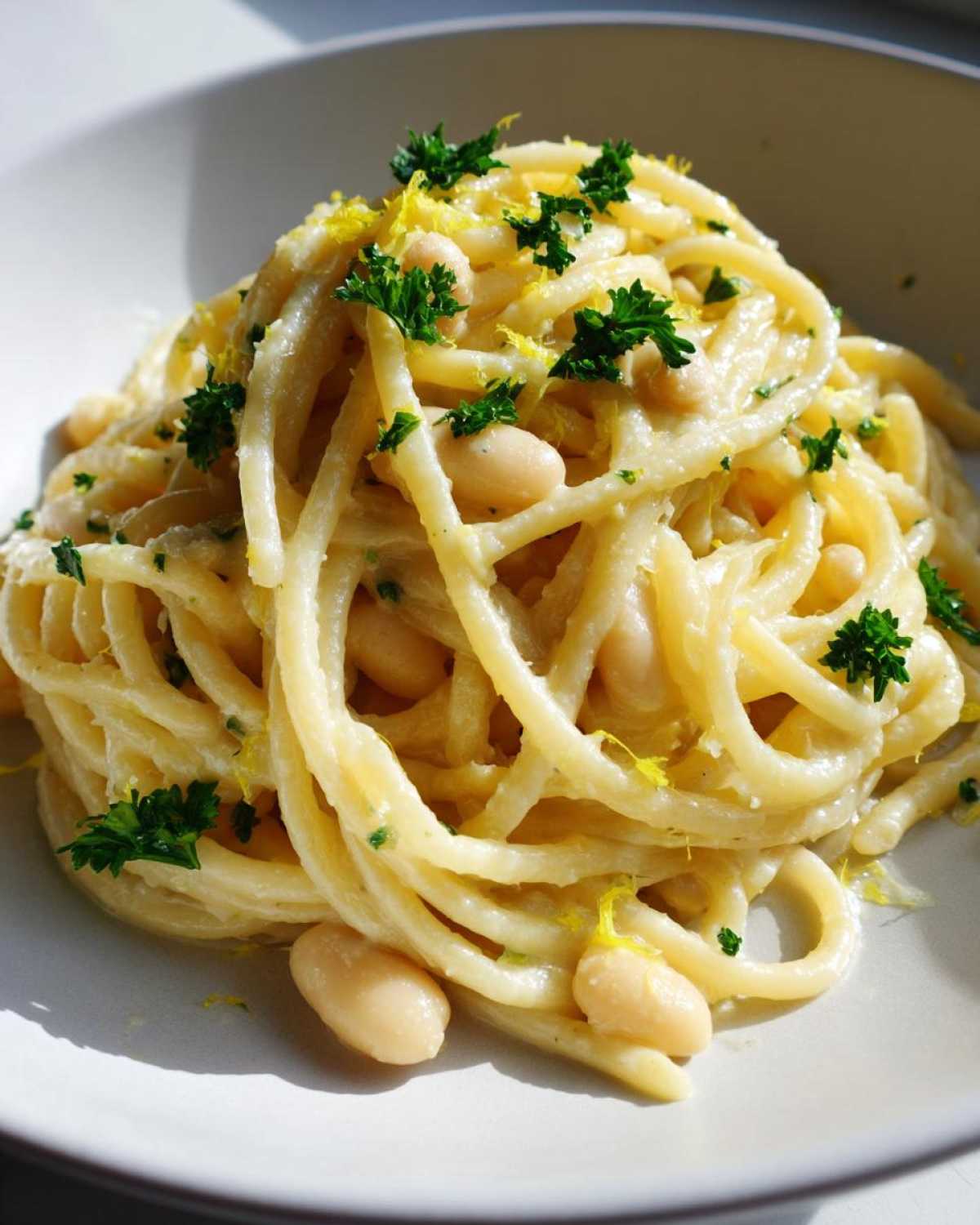 A close-up serving of One-Pot Creamy White Bean Lemon Pasta, topped with fresh parsley and lemon zest.