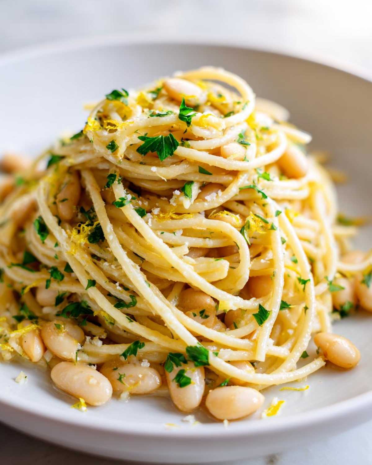 Close-up of a serving of One-Pot Creamy White Bean Lemon Pasta, topped with fresh parsley and lemon zest.