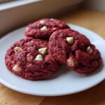 Three rich, red velvet cake mix cookies studded with white chocolate chips, resting on a white plate.
