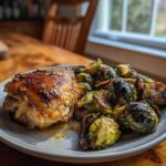 A serving of crispy Sheet Pan Garlic Butter Chicken and Brussels Sprouts on a light gray plate.
