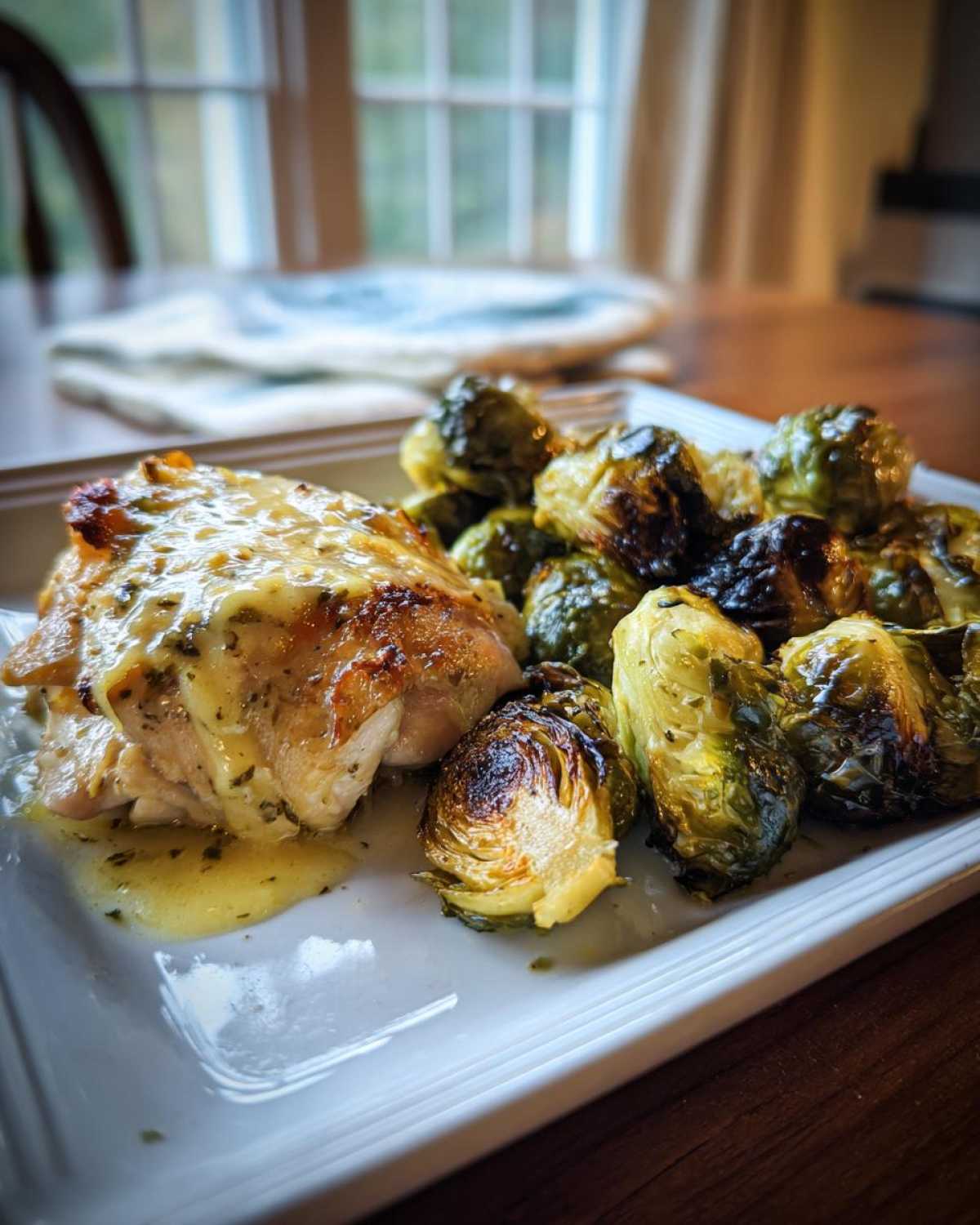 A serving of Sheet Pan Garlic Butter Chicken and Brussels Sprouts drizzled with sauce on a white plate.