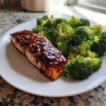 A close-up of a piece of Sheet Pan Honey Harissa Salmon with Broccoli served on a white plate.